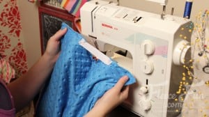 adding the elastic to the cape. I love this cute easy superhero cape DIY! It goes around the arms and not the neck for safe play - plus you can turn it around to be a blanket for baby! Easy sewing idea.