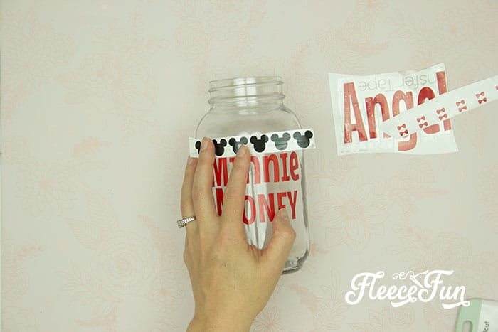 Carefully aligning vinyl on a Disney-themed savings jar using fleecefun and free template and tutorial