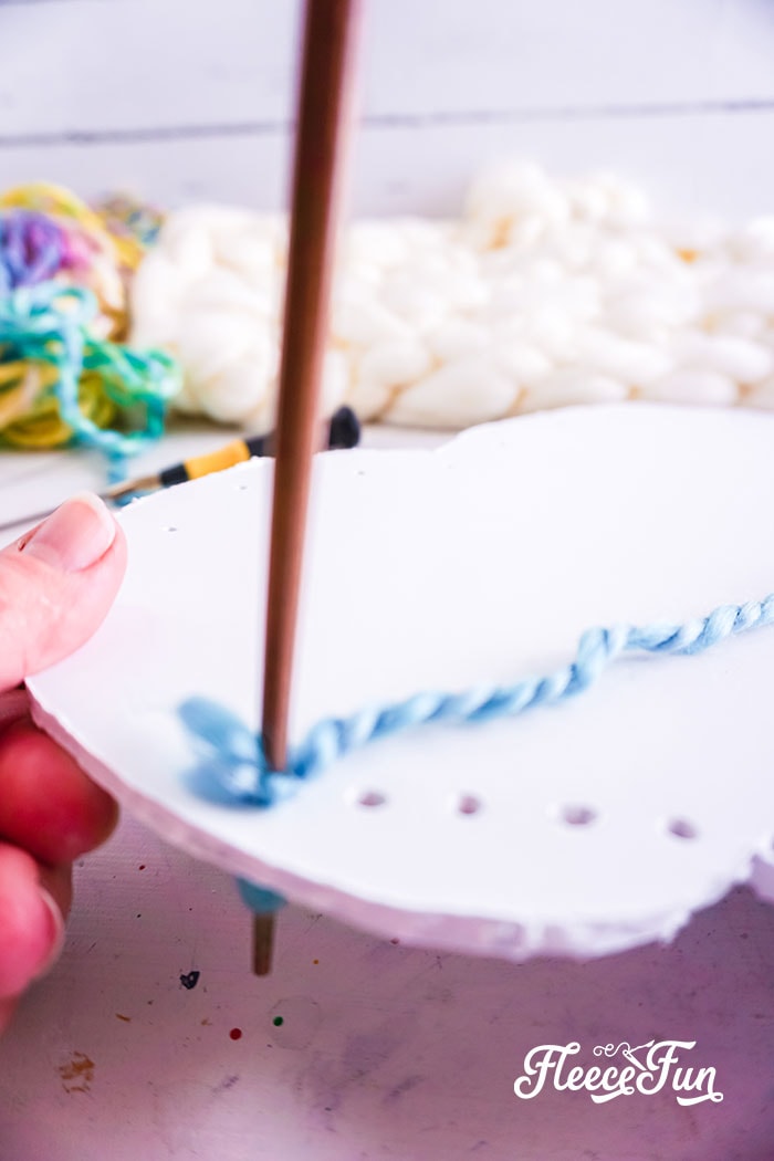 threading a piece of  rainbow yarn at the holes at the bottom of the cloud
