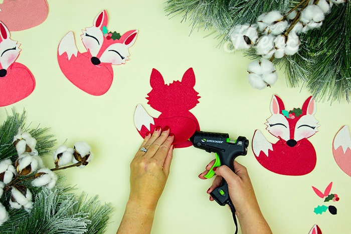 Gluing the tail on. This adorable Felt Fox Ornament DIY (Free Pattern) is a fun addition to your Christmas tree Ornaments!  Curled up in it's tail with a bit of holly on it's head this fox is the embodiment of merriment.  Use for tree decorations or as a fun addition to a wrapped gift.  Also makes a wonderful hostess gift or prize at a holiday party. Perfect handmade ornament to make.