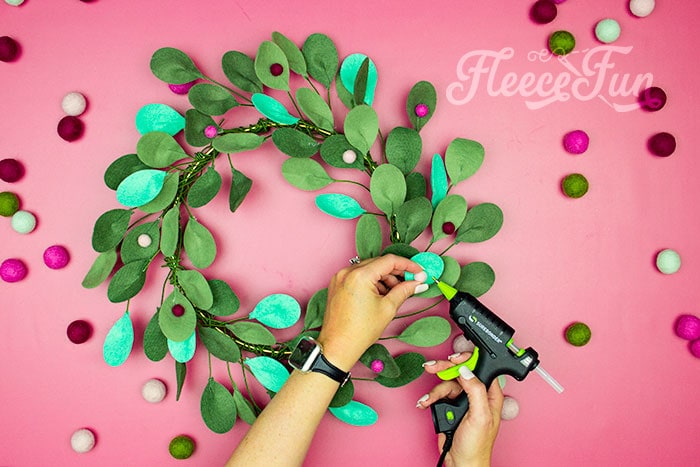 Adding felt pompoms as berries to the holiday wreath. This modern Christmas Wreath DIY (made from felt) is a whimsical addition to your holiday décor. With a few items you can make this festive wreath. Because of the way it's constructed no two are alike. Make it as full or as thin as your taste's desire. Because it's made from felt, this wreath can be made in an array of colors to suit your style.