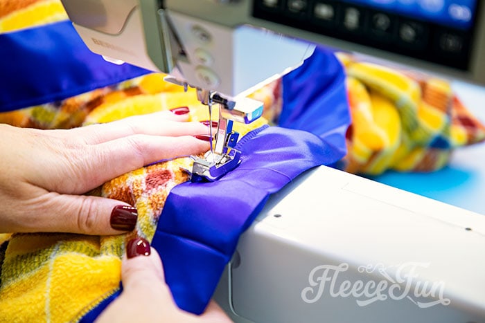 Sewing on using zig zag stitch to finish binding. Learn how to make a fleece blanket with satin binding! This tutorial is a perfect beginning sewing project! Learn how to make mitered corners.
